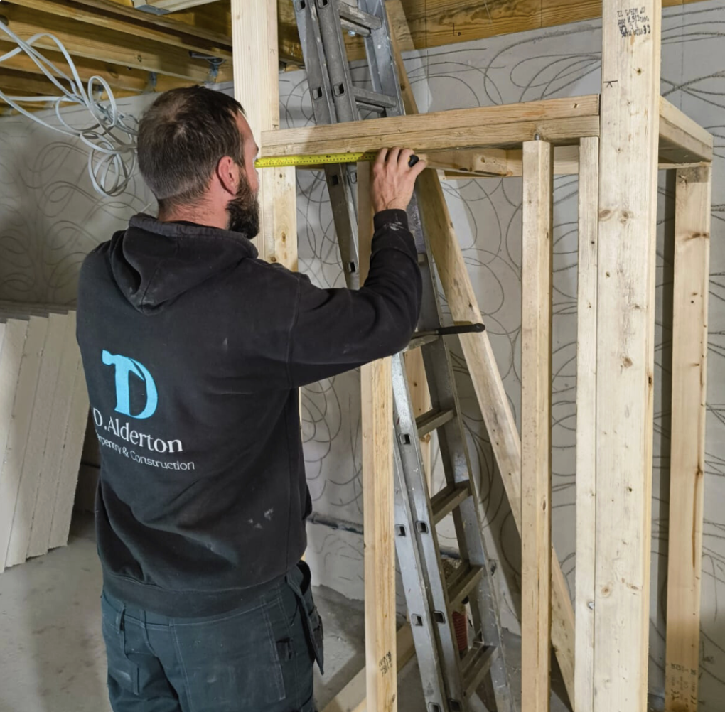 Dan Alderton on site — measuring a timber stud frame in Guernsey